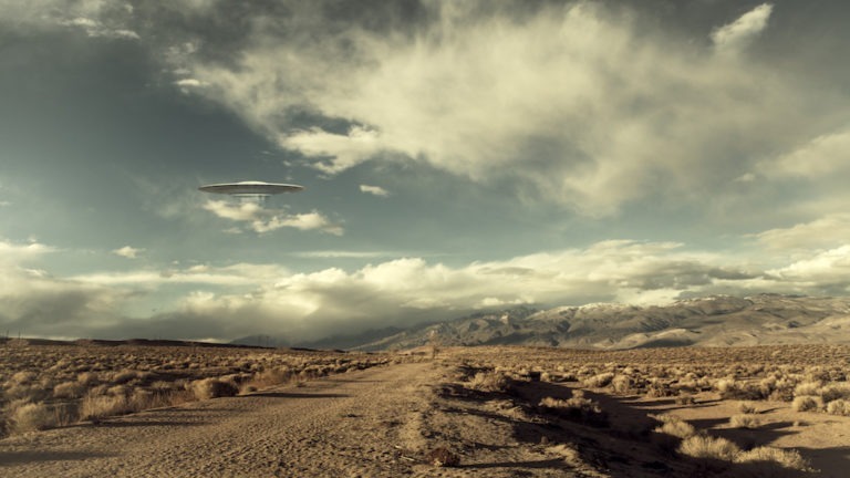 UFO spaceship hovering over a desert road with puffy clouds processed with a vintage look.